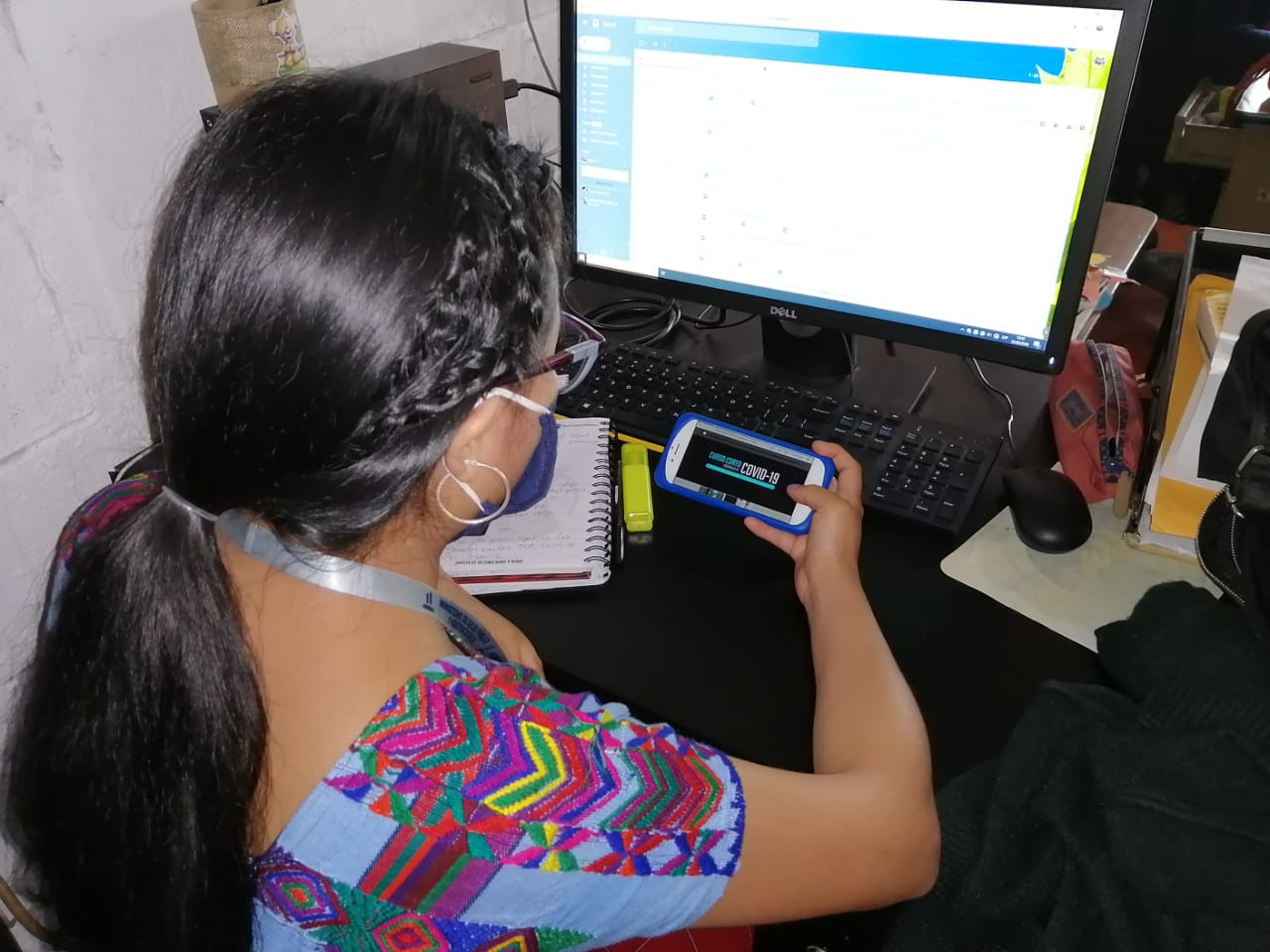 Health worker at desk uses her mobile telephone to watch micro-training course on COVID-19.